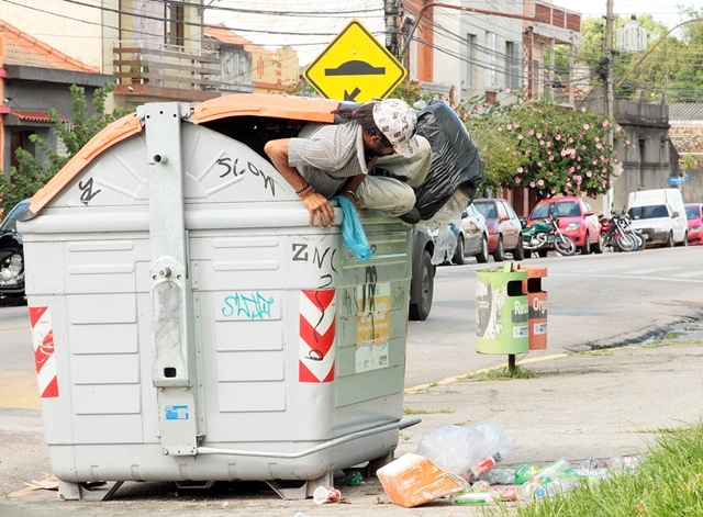 Catador procura alimento dentro de container de lixo orgânico.