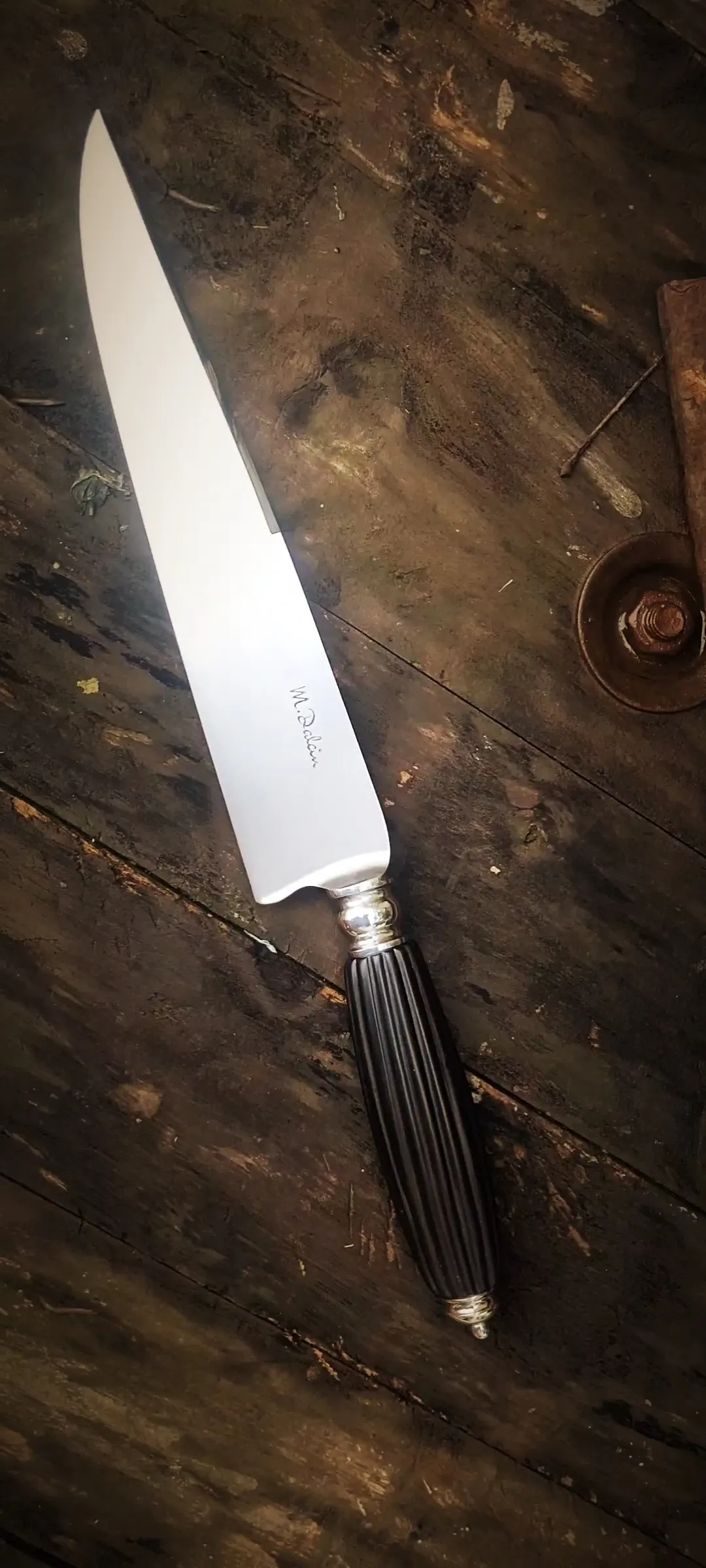 A NĀLU: forjada em aço carbono 52100, com 24 cm de lâmina e cabo de ébano indiano, assinada M. Dalcin.